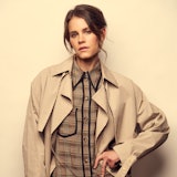 A portrait of Sosie wearing a trench coat and plaid mini dress
