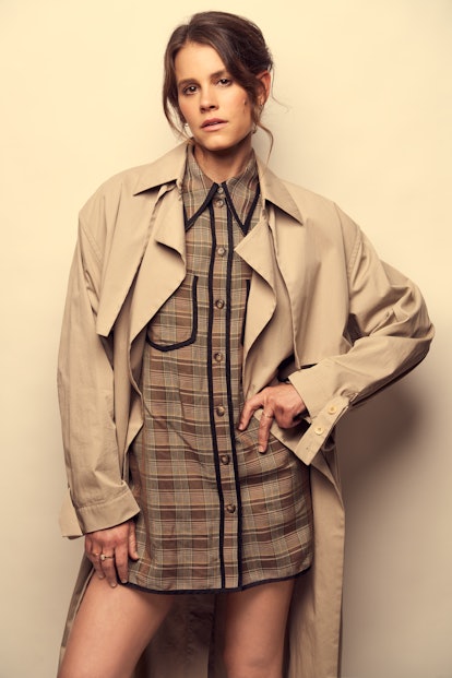 A portrait of Sosie wearing a trench coat and plaid mini dress