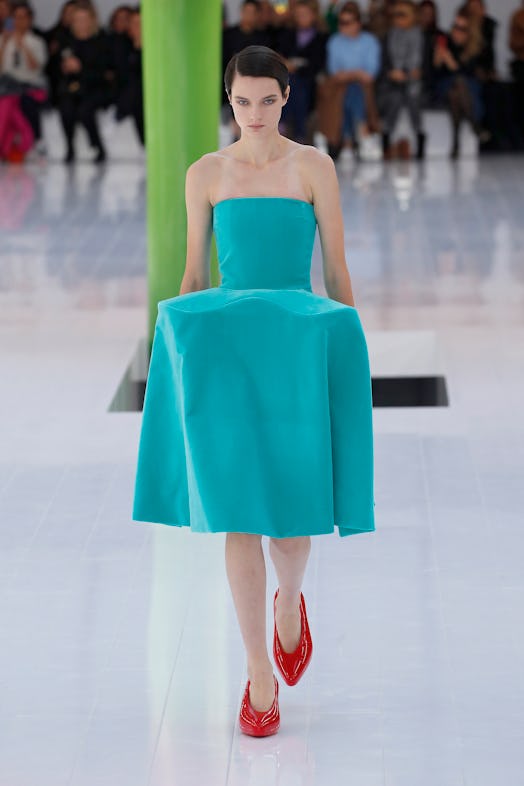 A model walking the runway in a turquoise dress and red shoes at Loewe Spring 2023 Paris Fashion Wee...