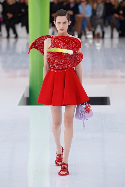 A model walking the runway in a red dress with a giant red flower over her torso at Loewe Spring 202...