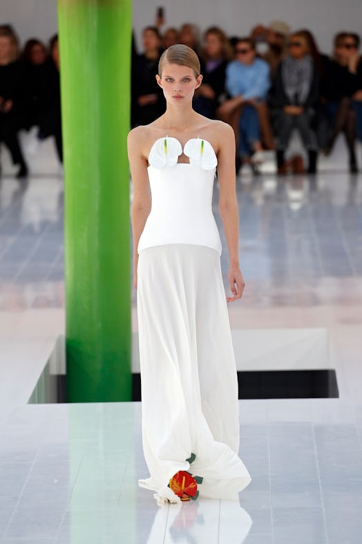 A model walking the runway in a white dress with flowers as a bra at Loewe Spring 2023 Paris Fashion...