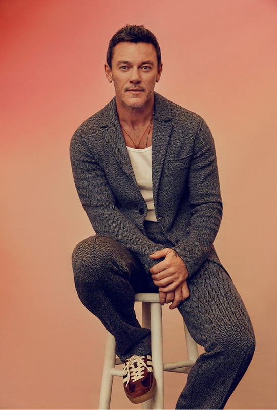 Luke Evans sitting on a high chair in a Missoni jacket and pants, a Calvin Klein tank top and Adidas...