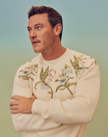 Luke Evans posing in a white Dior Men sweater with flowers on it, looking into the distance 