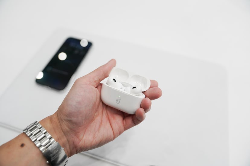 Apple's AirPods Pro 2 pictured in hand against the backdrop of a white table