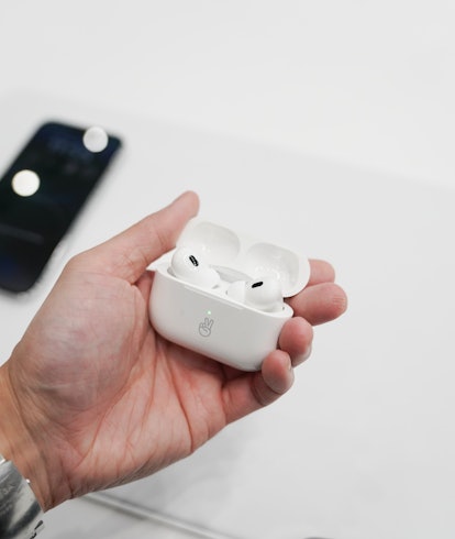 Apple's AirPods Pro 2 pictured in hand against the backdrop of a white table