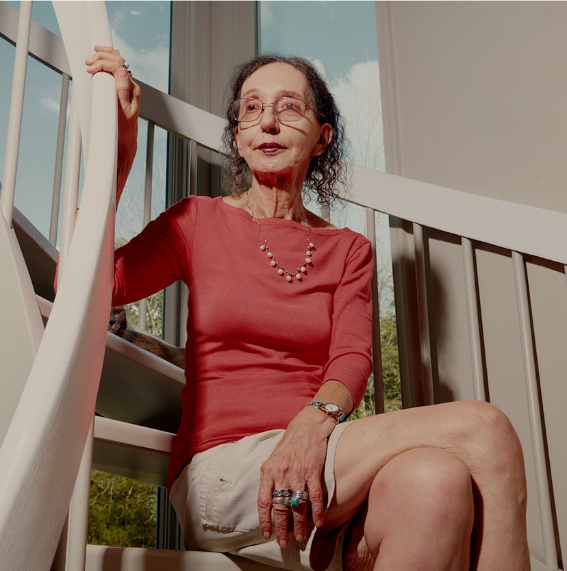 Joyce Carol Oates sitting on stairs in a coral shirt and beige skirt