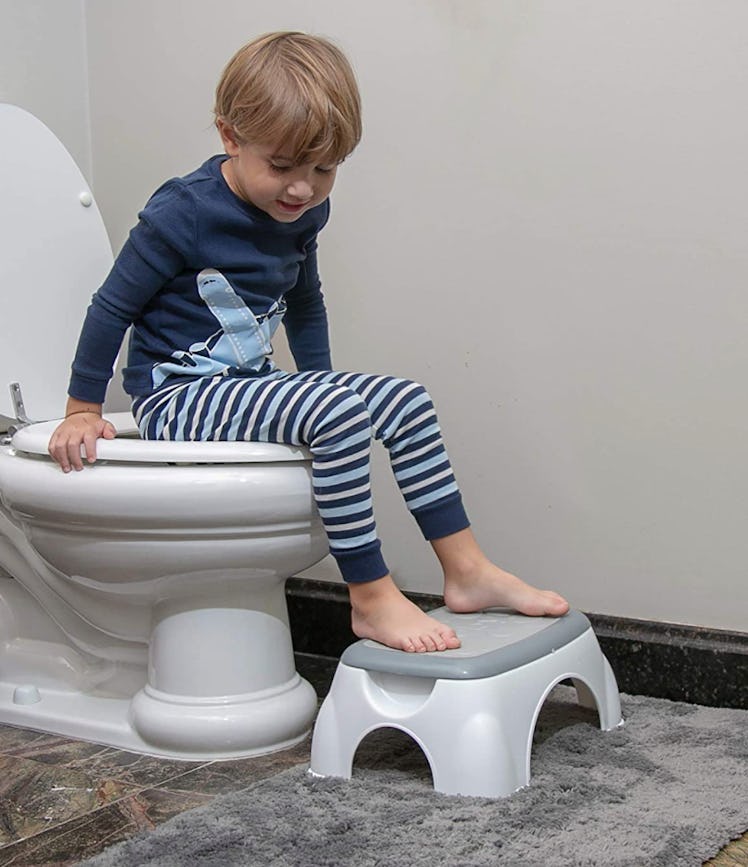 Little boy in pajamas sitting on toilet with feet on gray and white Nuby step stool