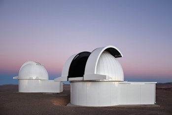 Color photo of two observatory domes with a sunset sky in the background