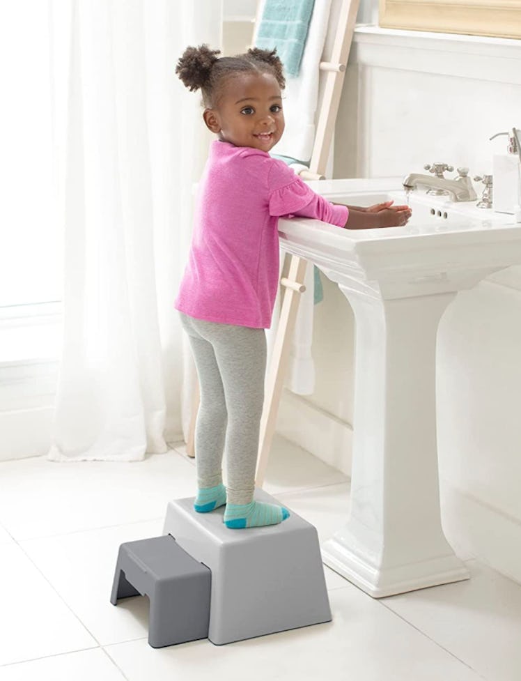 Toddler girl washed hand while standing on gray step stool