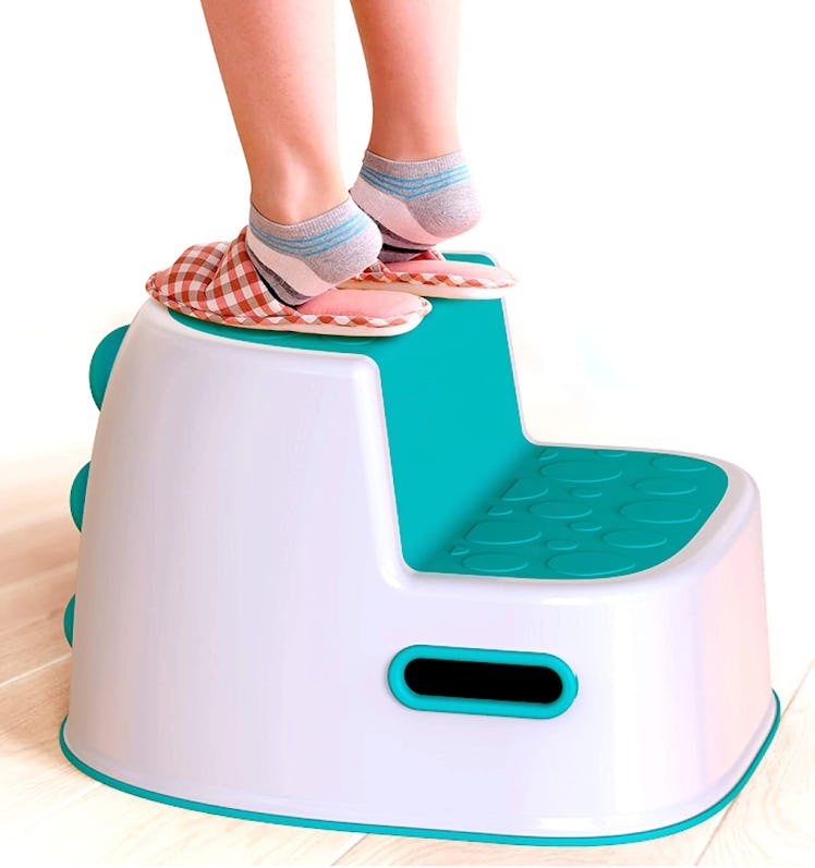 Child standing on white and teal dinosaur themed step stool 