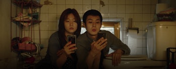 Siblings Ki-jung and Ki-woo crouch in semi-basement
