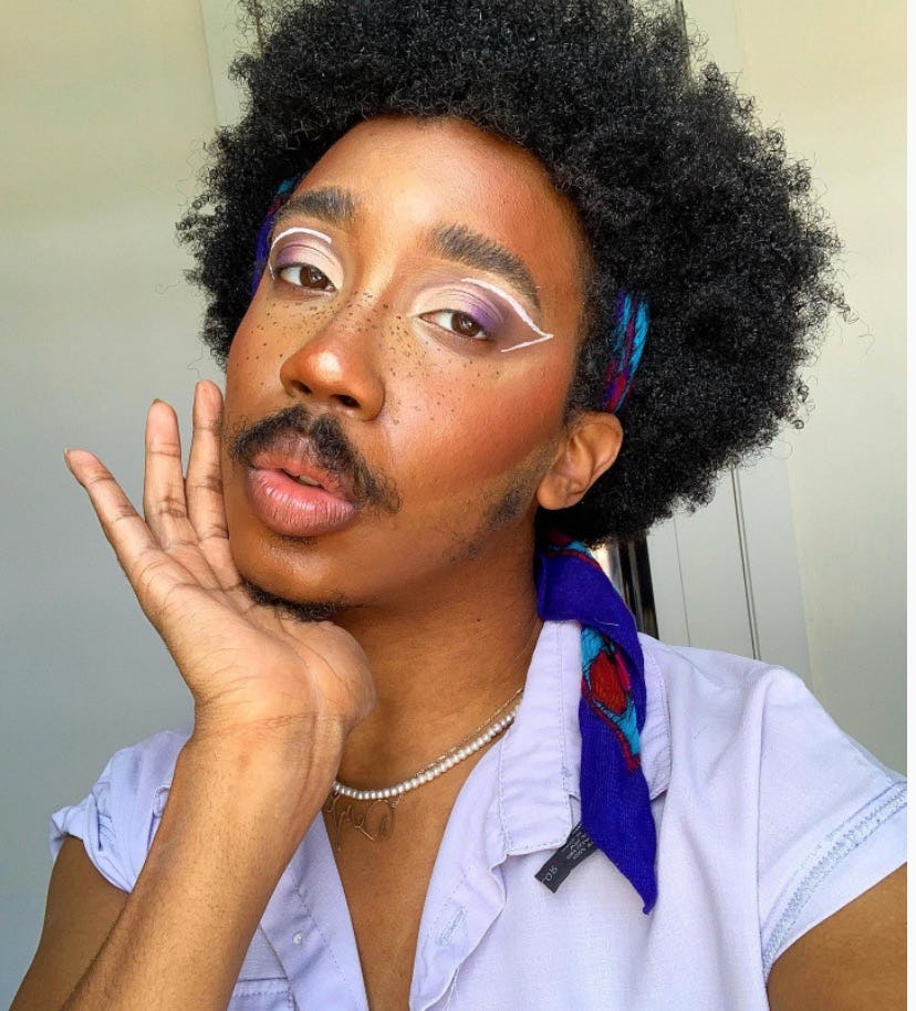 Dezi Tibs, a trans person, wearing a light blue shirt, a dark blue headband and a pearl necklace