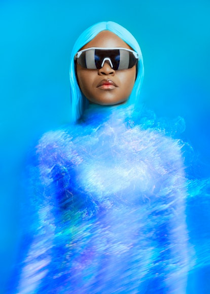 A portrait of Sampa the Great in a blue, bodysuit and blue hair with futuristic shades.