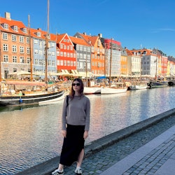 Courtney Falsey wearing a black skirt and a grey shirt while posing in Nyhavn 