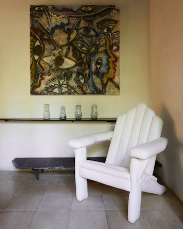 Inside the room of the Rose House, a white chair, a low black table, a shelf with vases, and eye-the...