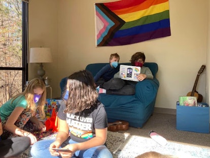 Four students from Georgia school wearing face masks, sitting around in front of an LGBTQ+ flag.