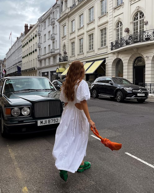 A brunette woman walking down a street in a white dress