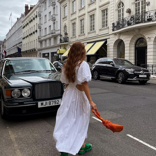 A brunette woman walking down a street in a white dress