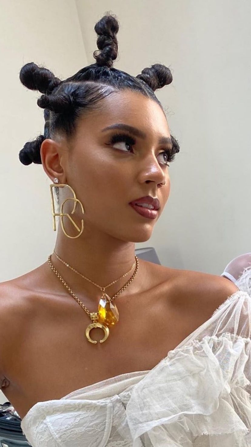 A Black woman wearing bantu knots and a brick red lip.