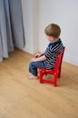 一个孩子在休息时坐在面向角落的椅子上。