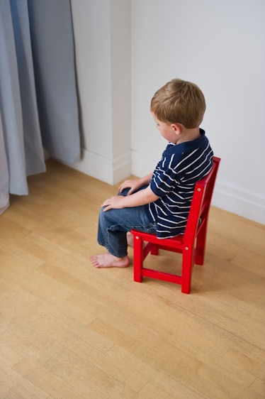A child sitting in a chair facing a corner during a timeout.