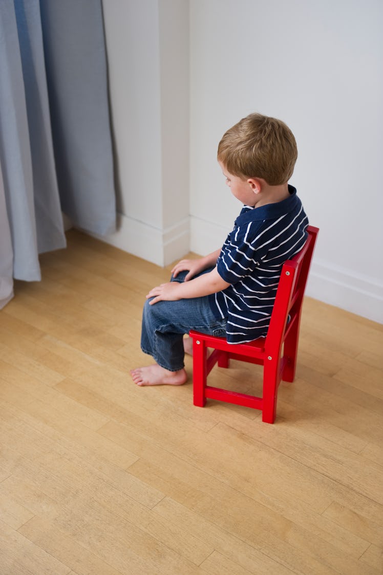 A child sitting in a chair facing a corner during a timeout.