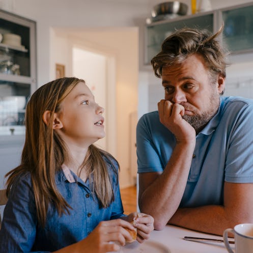A daughter and father talking at a table at home.