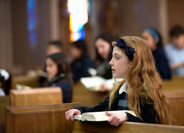一个女孩在天主教的宗教仪式上坐在教堂的长椅上。