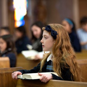 A girl in a church pew at a Catholic religious service.