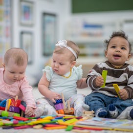 Three babies sitting up and playing with toys.