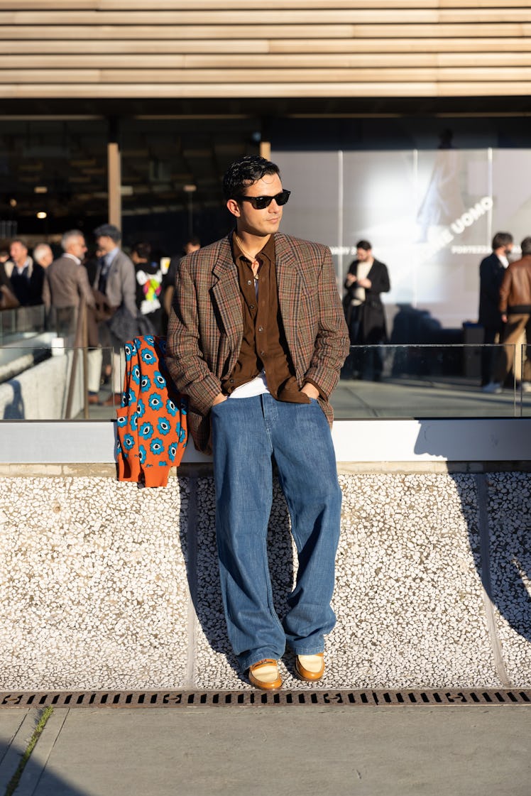 Alessandro Enriquez wearing large denim pants, a suede brown button shirt, a checkered blazer jacket...
