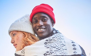 A man wearing a red beanie while hugging his girlfriend