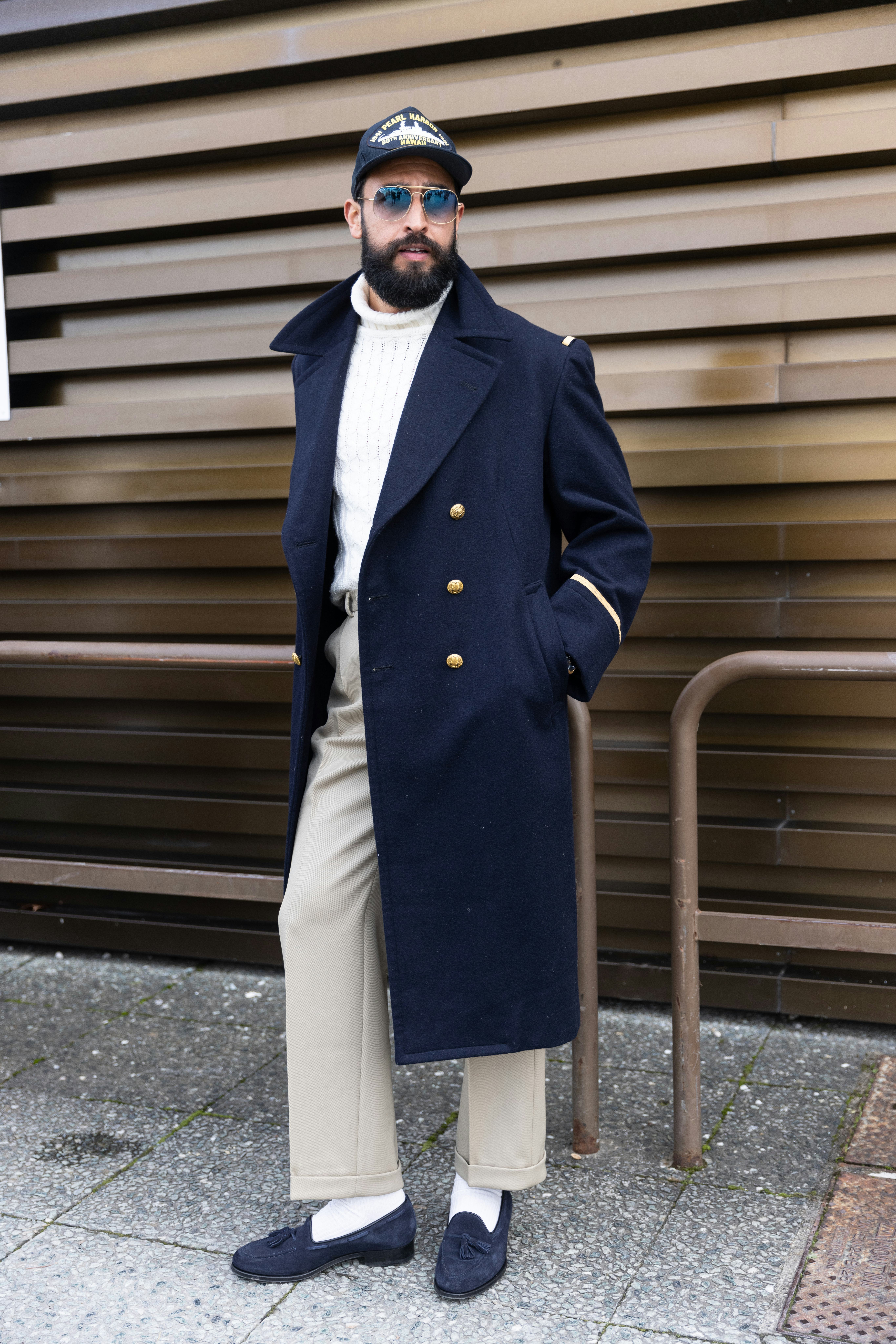 A guest wearing a Pearl Harbor commemoration baseball cap, a long coat and white ribbed sweater at F...