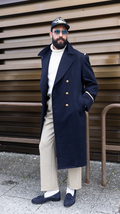 A guest wearing a Pearl Harbor commemoration baseball cap, a long coat and white ribbed sweater at F...