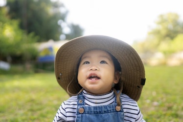 An April baby looks into the sky outside in a grassy field.