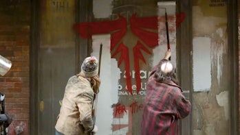Two people paint over some Fireflies graffiti in HBO’s The Last of Us.