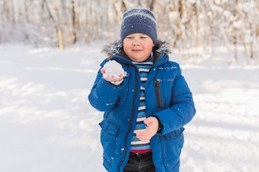A fat child holding a snowball while outside playing in the snow.
