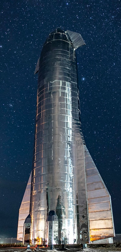 SpaceX's giant Starship launch vehicle towers over the land with glowing stars in the background aga...