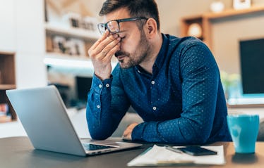 A sleep-deprived man at work holding his head in his hands.