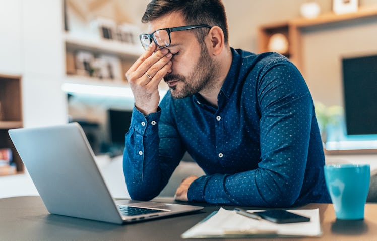 A sleep-deprived man at work holding his head in his hands.