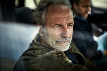 A confident man sitting in the passengers seat of a car looking out the window