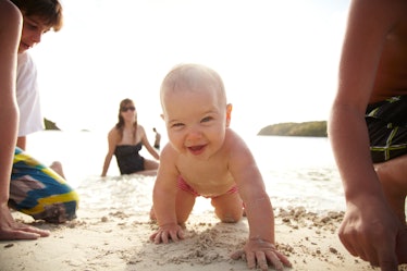 A baby crawling toward the viewer on a sandy beach.