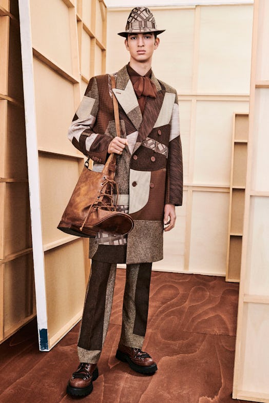 a model wearing a patchwork suit carring a large purse shaped like a boot