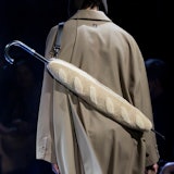 a model seen from behind wearing an umbrella strapped across his back that's encased in a shearling ...