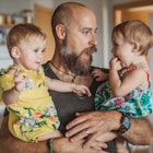 A father holds his two baby daughters and makes a silly face.