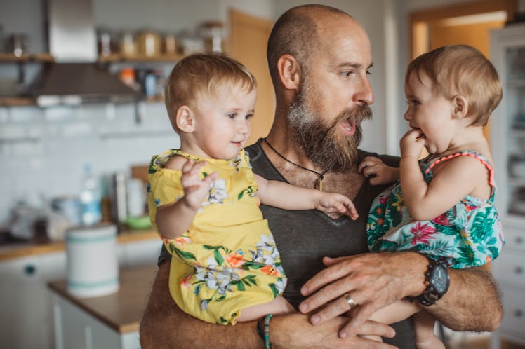 A father holds his two baby daughters and makes a silly face.