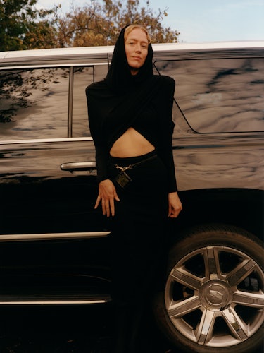 Raquel Zimmermann wears a black dress, belt, and boots