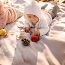 Two babies in onesies on a blanket on a pile of leaves in autumn.