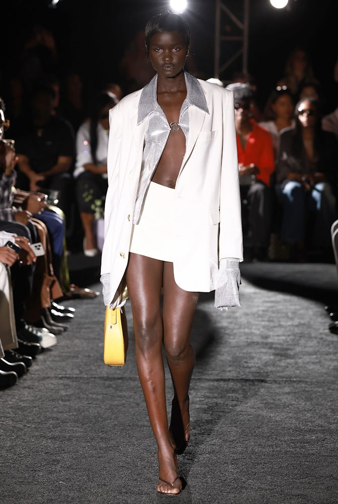 Model Akon wears a white mini skirt, blazer, and yellow bag.
