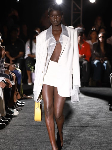 Model Akon wears a white mini skirt, blazer, and yellow bag.